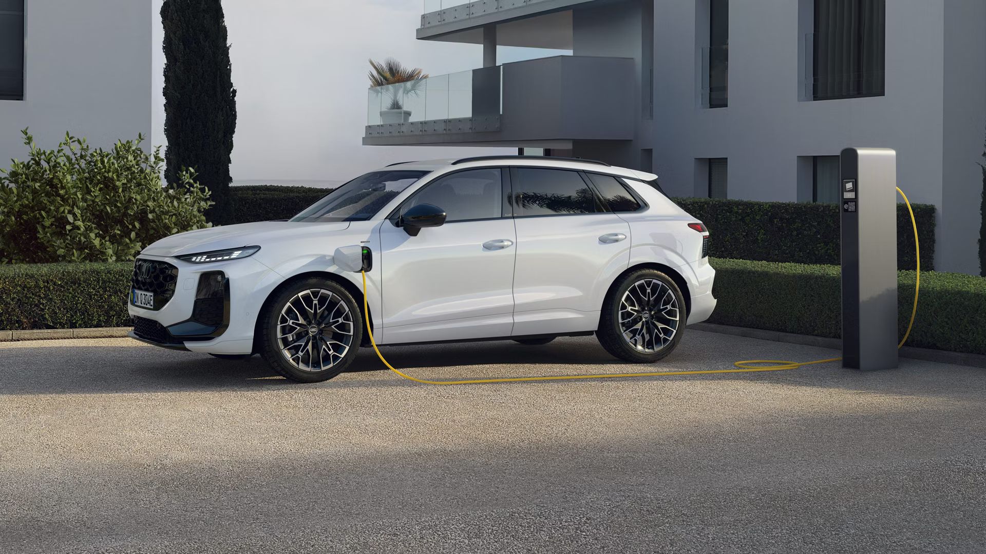Weißer Audi Q3 SUV e-hybrid steht an der Ladesäule vor einem Gebäude