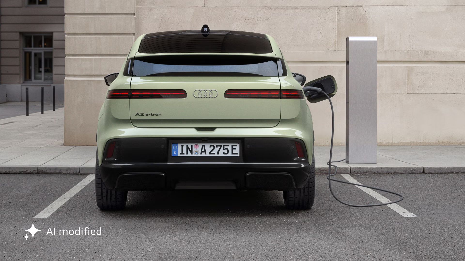Der Audi A2 e-tron, schräg von vorne fotografiert, parkt vor einem modernen Gebäude mit Wänden in Steinoptik. Das Fahrzeug ist an eine Ladesäule angeschlossen.