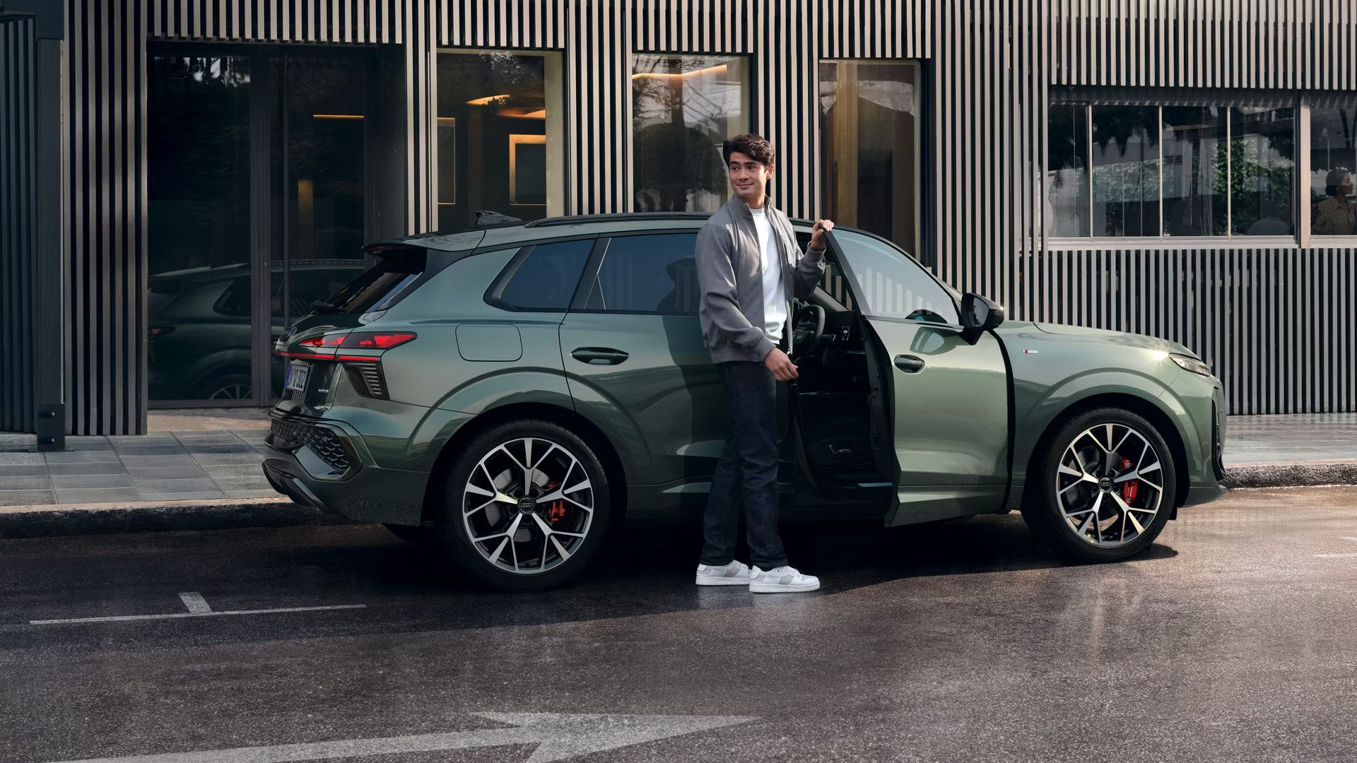 Ein Mann steht an der offenen Beifahrertür eines Audi Q3 SUV, der vor einem Gebäude parkt.