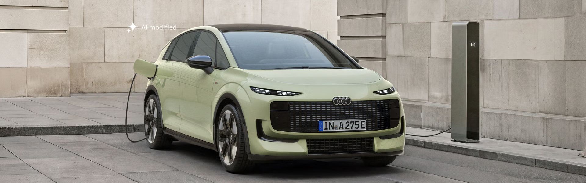 Der Audi A2 e-tron, frontal von hinten fotografiert, parkt vor einem modernen Gebäude. Das Fahrzeug ist an eine Ladesäule angeschlossen.