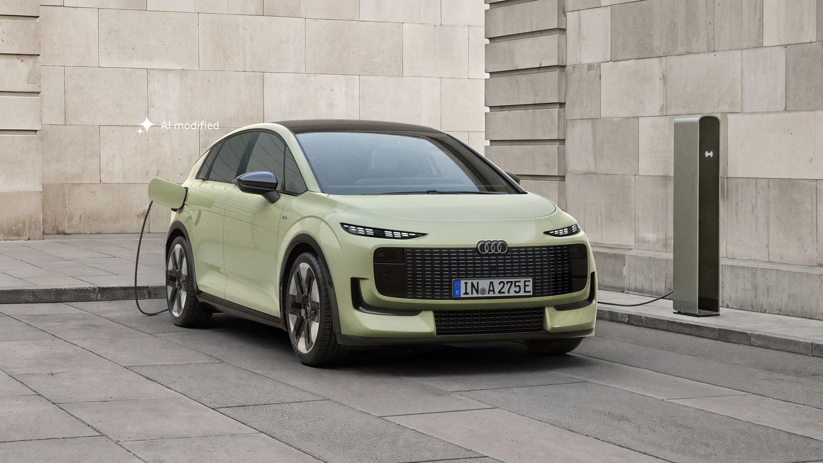 Der Audi A2 e-tron, frontal von hinten fotografiert, parkt vor einem modernen Gebäude. Das Fahrzeug ist an eine Ladesäule angeschlossen.